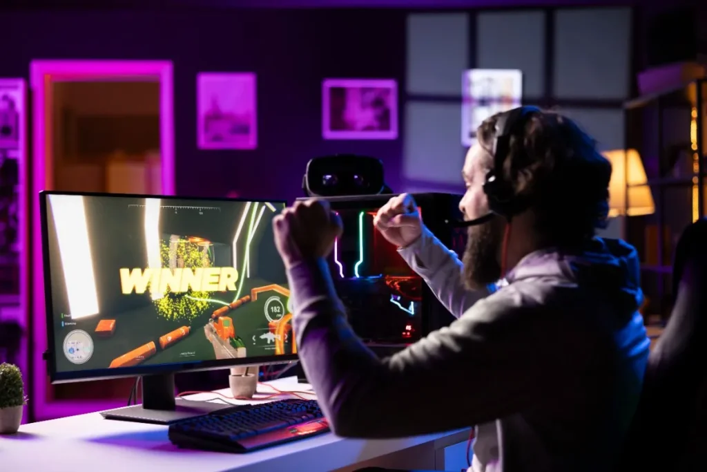 Aeonscope video gaming esports player celebrating victory at gaming setup with RGB lighting, gaming monitor displaying winner screen, headset, and colorful LED ambient lights in streaming room