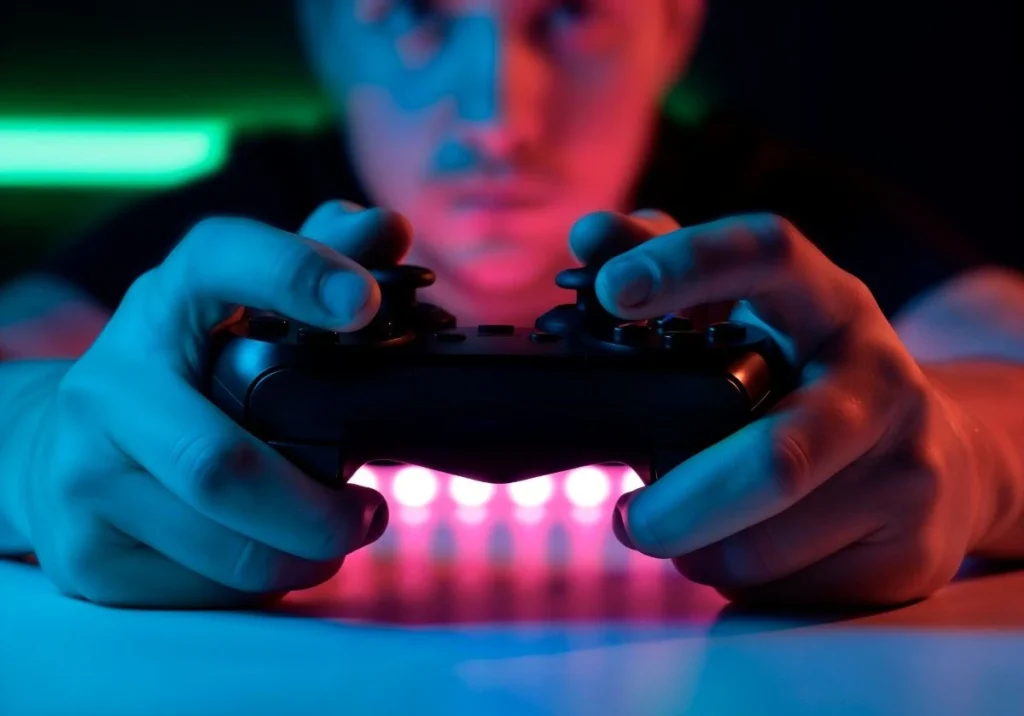 Gamer holding PS4 DualShock controller with glowing pink light bar showing active connection during PS4 gaming session at night