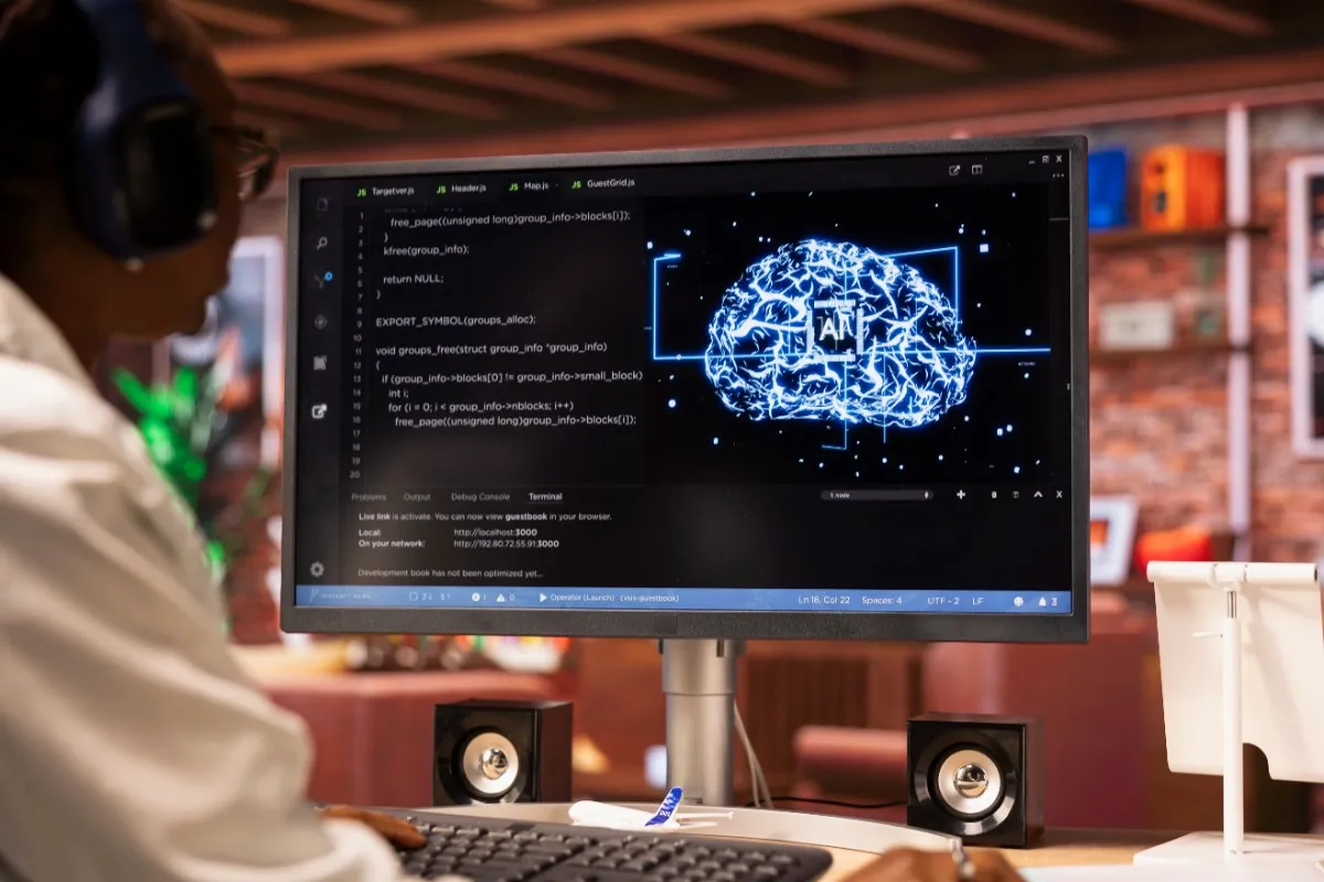 A remote software engineer working on a desktop computer with a glowing 3D neural network brain on screen, representing the backend development of ai bathroom design free software.