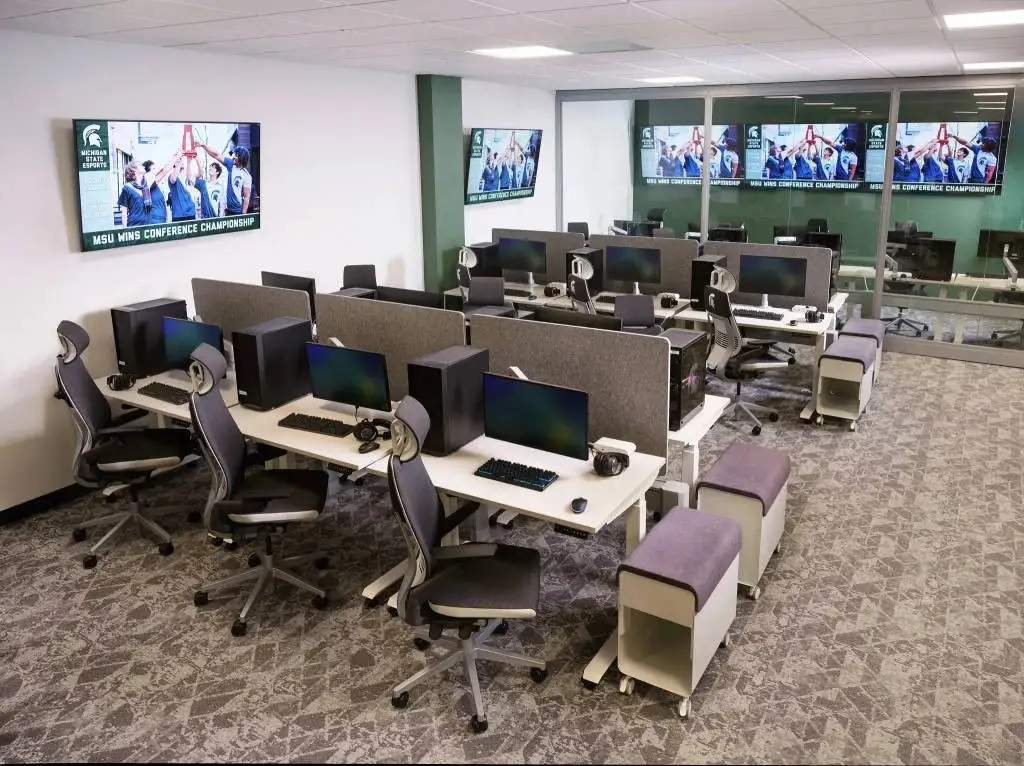 A high-angle look at an empty computer lab facility with dual rows of desk setups and wall-mounted screens highlighting an msu gaming conference championship win.