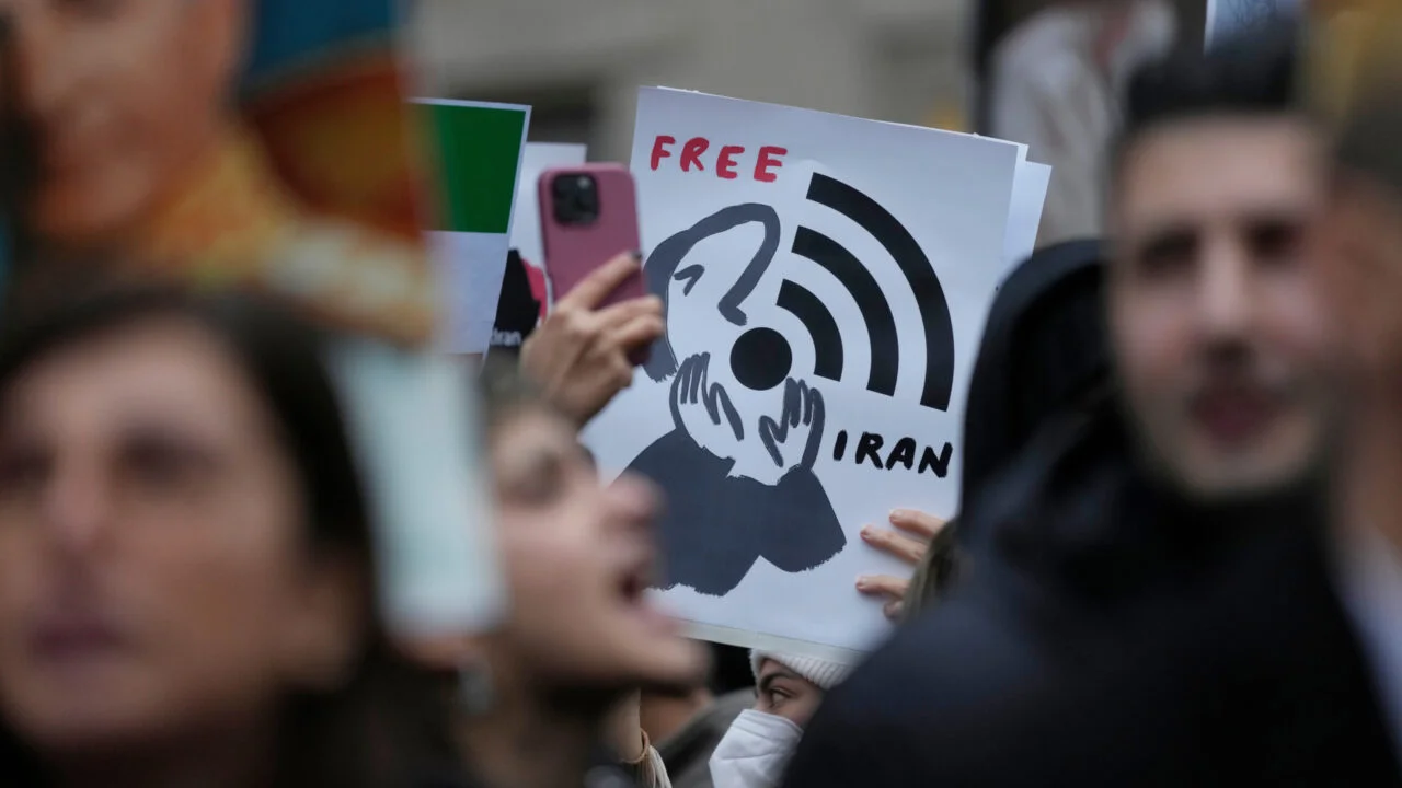 A demonstrator holds up a poster reading Free Iran with a graphic illustration highlighting censorship and the restriction of iran's internet access.